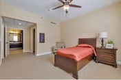 A spacious bedroom with a wooden bed, nightstands, lamps, a ceiling fan, and beige carpet.
