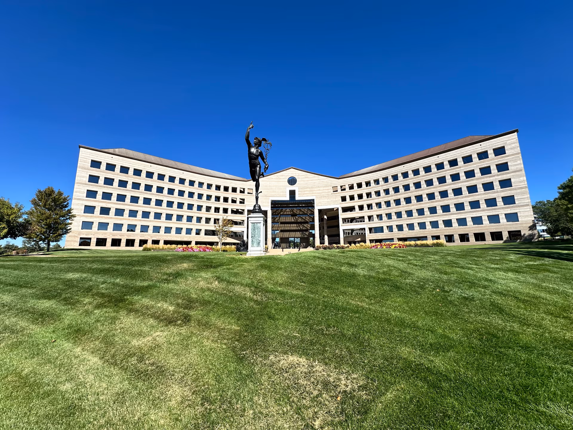 A large modern building with a central statue on a green lawn under a blue sky.