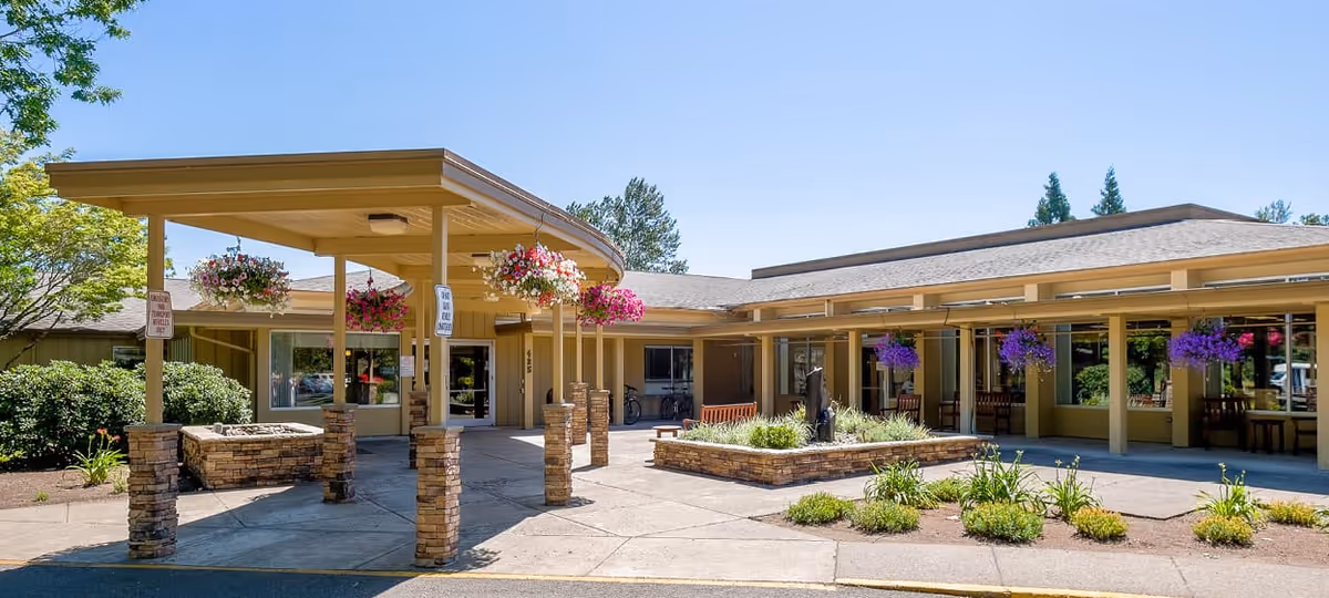 Exterior view of Avamere Riverpark of Eugene, with a covered entrance and hanging flower baskets.