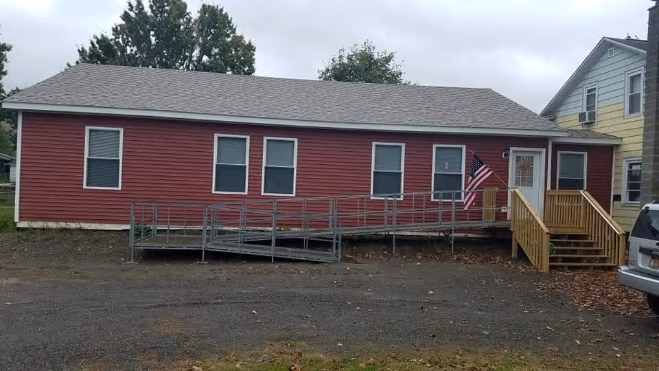 Red single-story building with wheelchair ramp, stairs, and an American flag at the entrance.