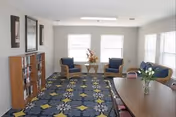 Cozy senior living lounge with blue chairs, sofas, and a patterned rug.