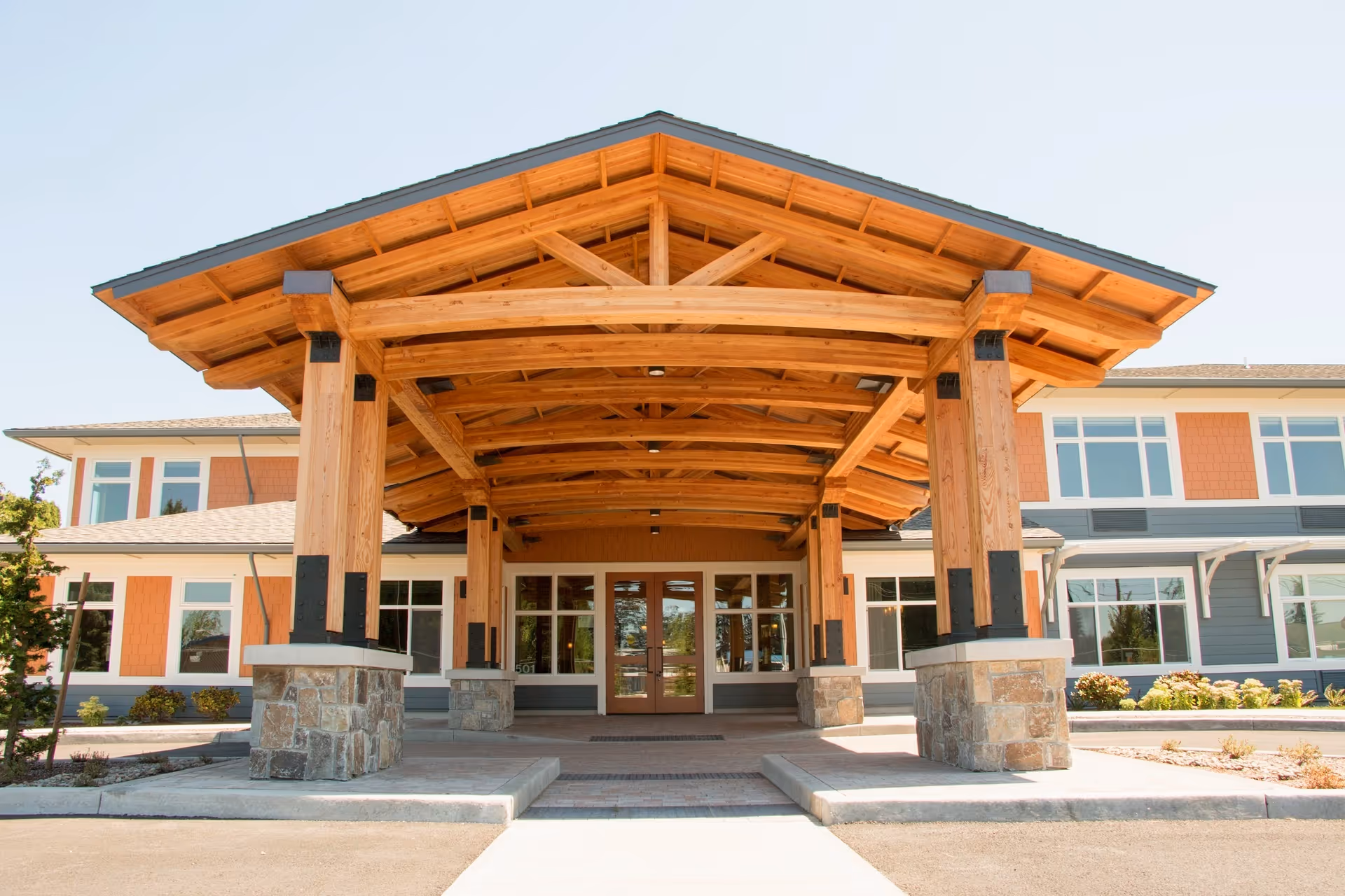Wooden covered entrance with stone columns leads to a modern senior living facility.