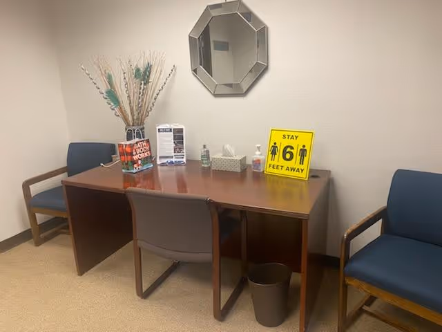 Interior waiting area with a table, chairs, brochures, and a Stay 6 feet away sign.