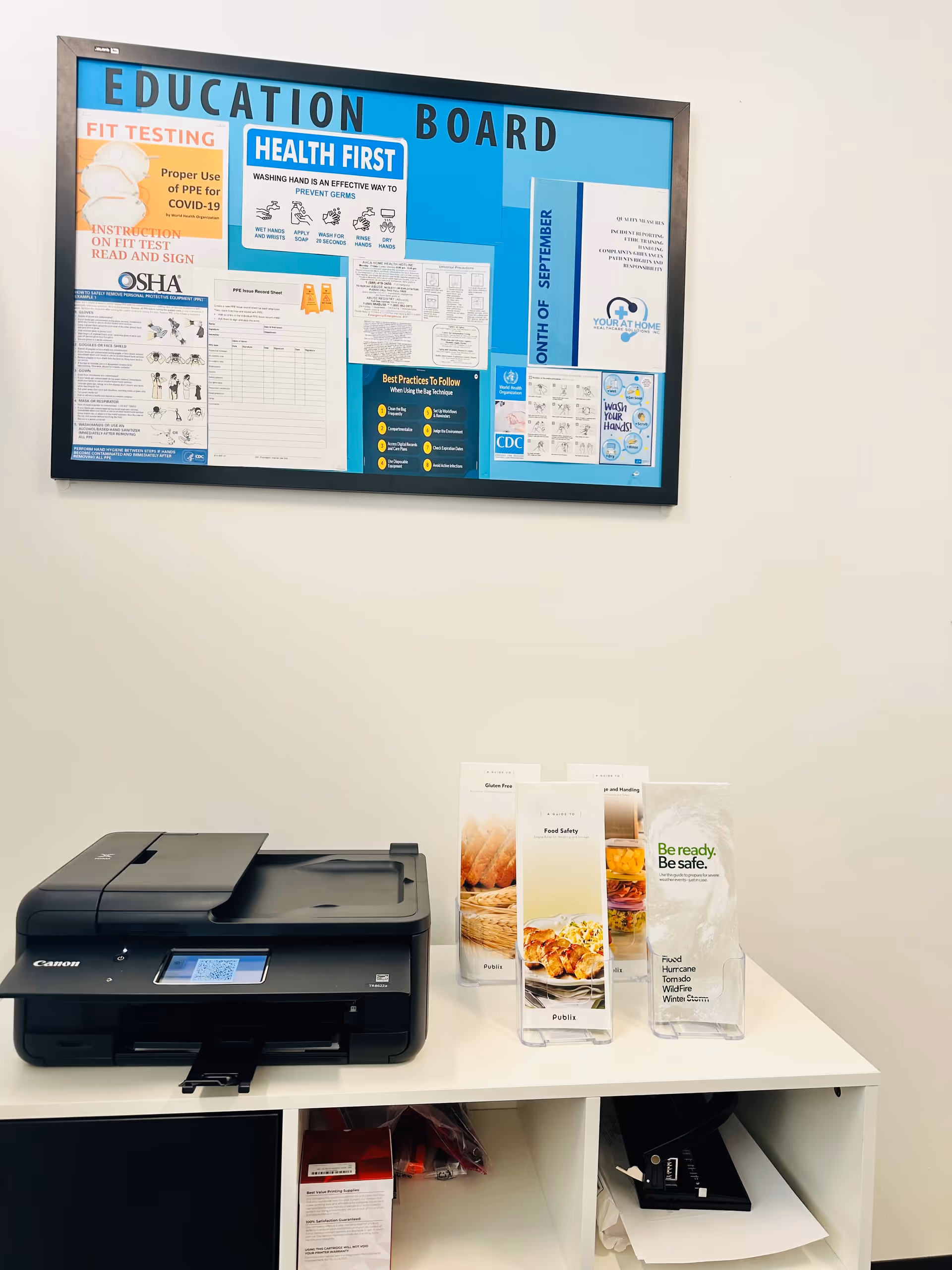 Inside a facility, a blue education board hangs above a white counter with a printer.