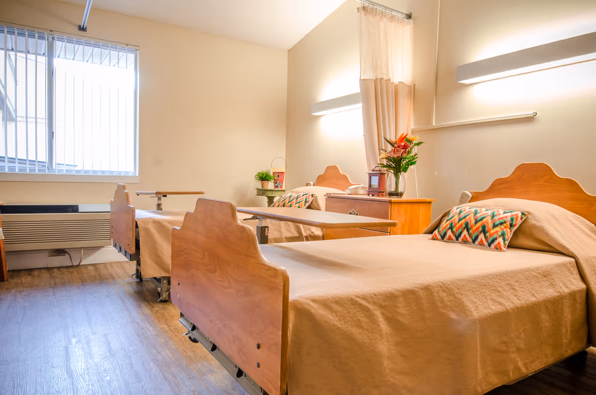 Two single beds with beige bedding in a sunlit senior living bedroom.