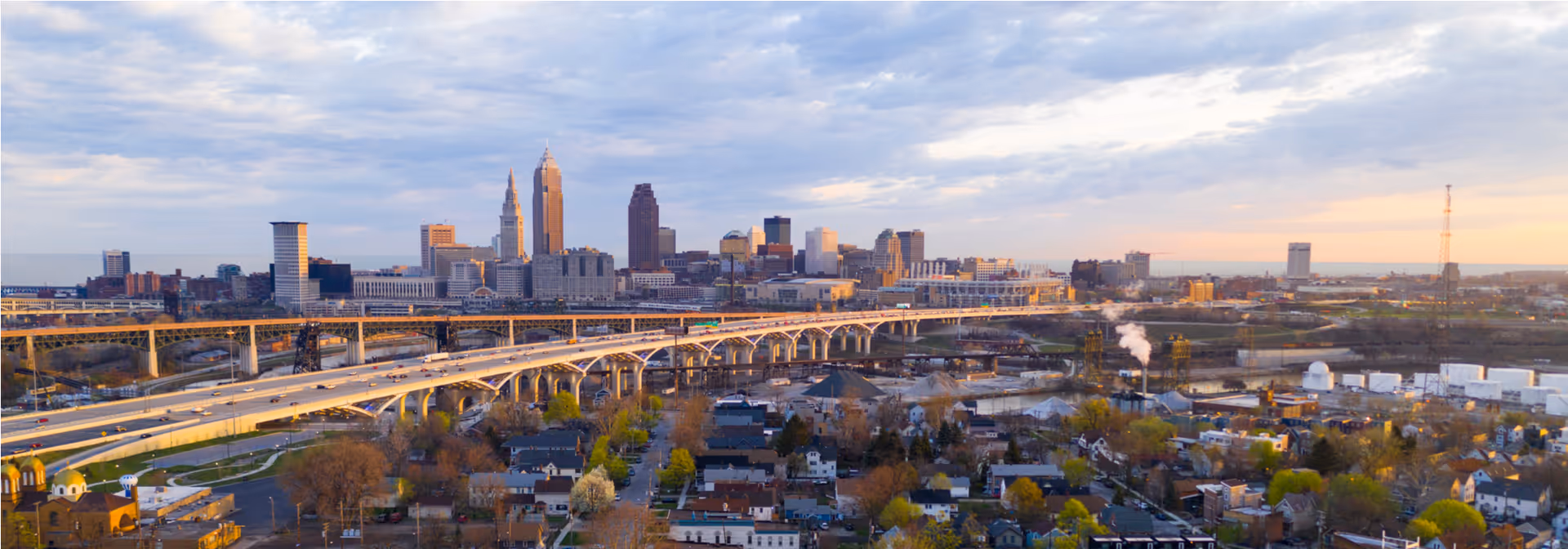 Aerial cityscape featuring a river, several bridges, and a distant skyline at dusk.