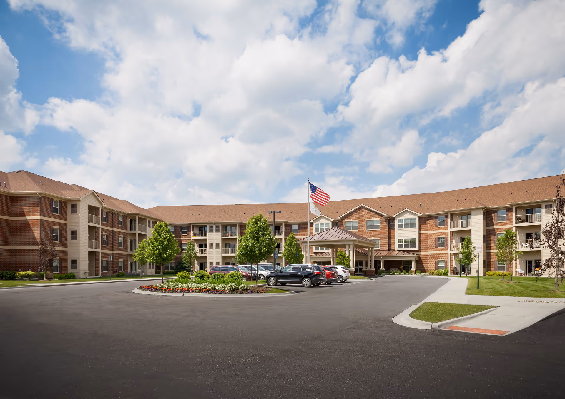 Exterior view of a Pomeroy Living Rochester Independent facility with entrance, flag, and parking.