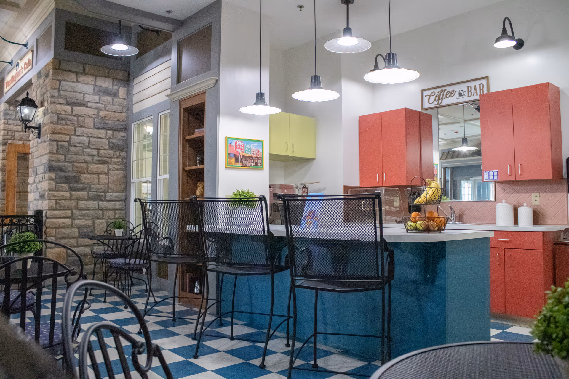 Bright communal kitchen with blue island, red cabinets, bar stools, and a coffee bar sign.
