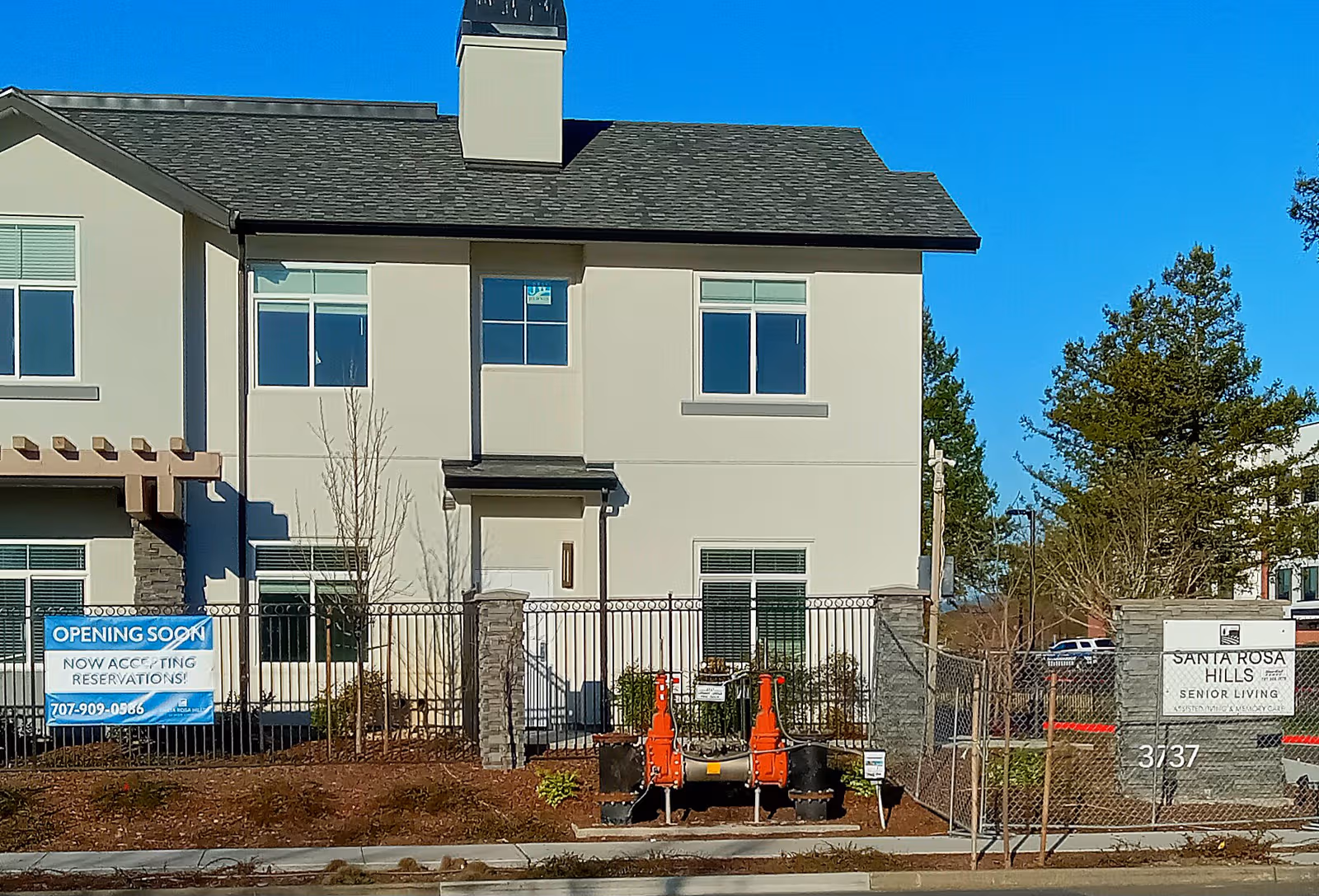 Two-story beige Santa Rosa Hills senior living building front under construction, fenced with signage