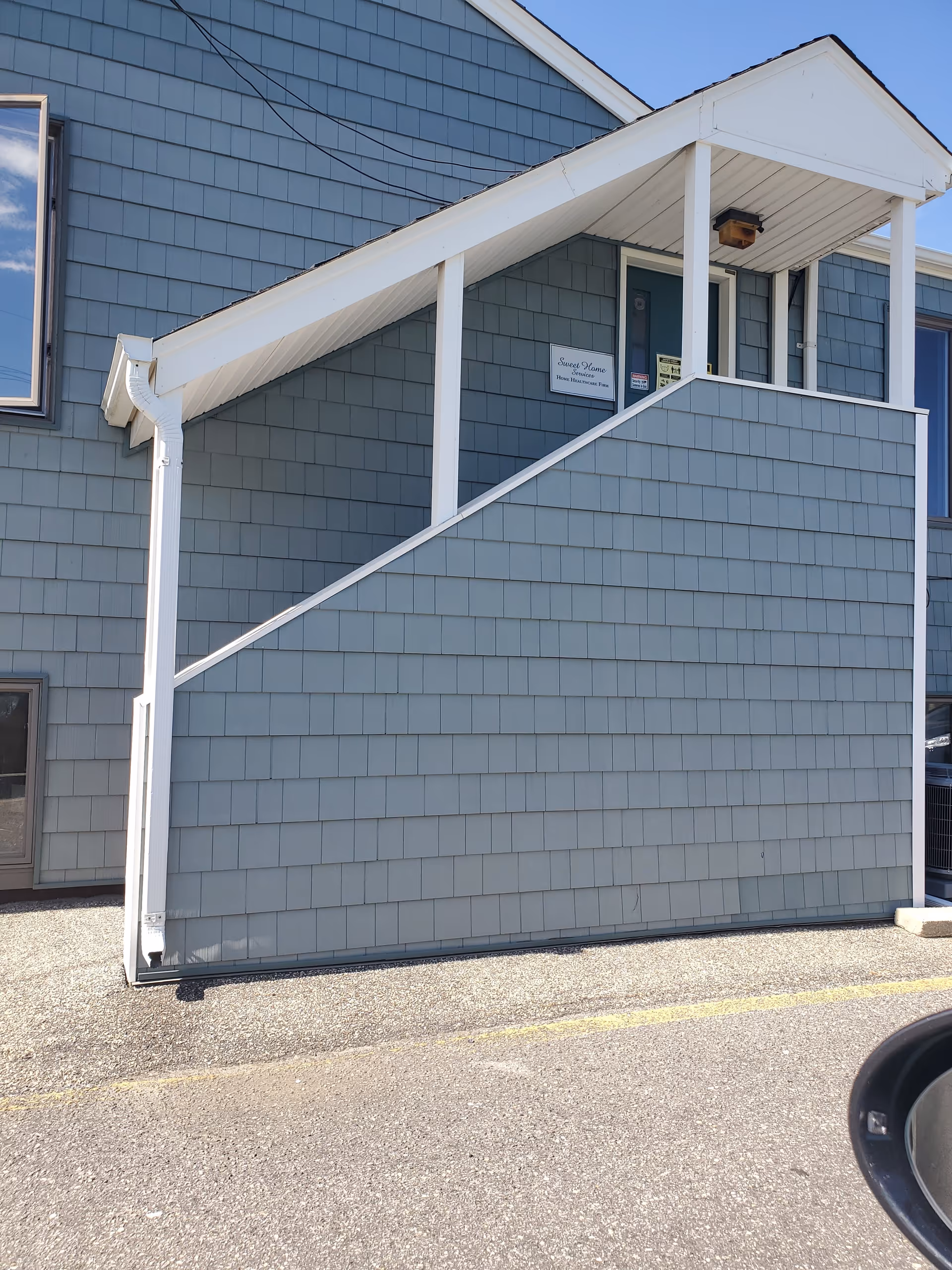 Exterior of a blue-shingled senior care facility with a small covered entry and stairs.