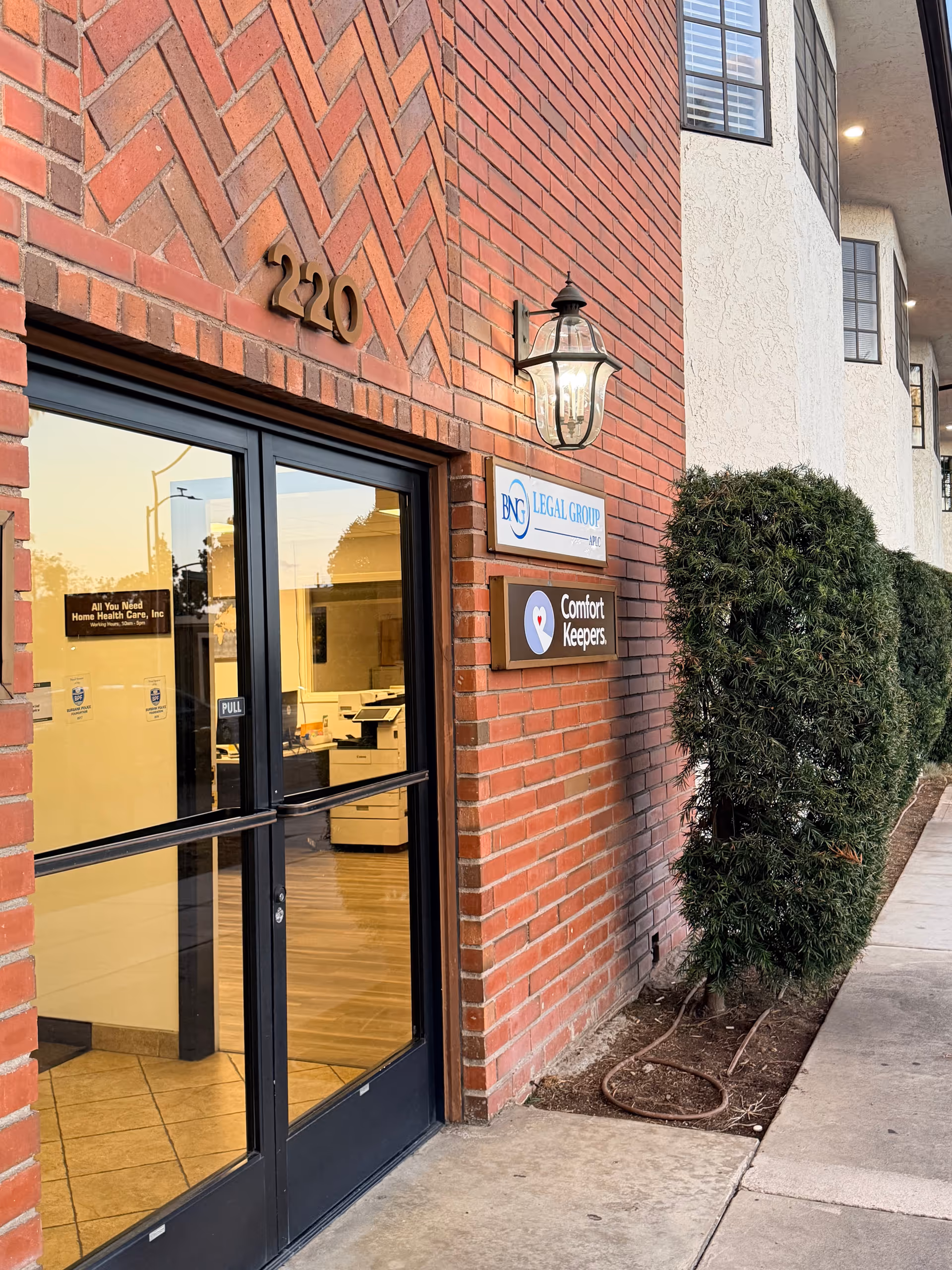 Brick building entrance with glass doors, address 2220, signs for Comfort Keepers and legal group.