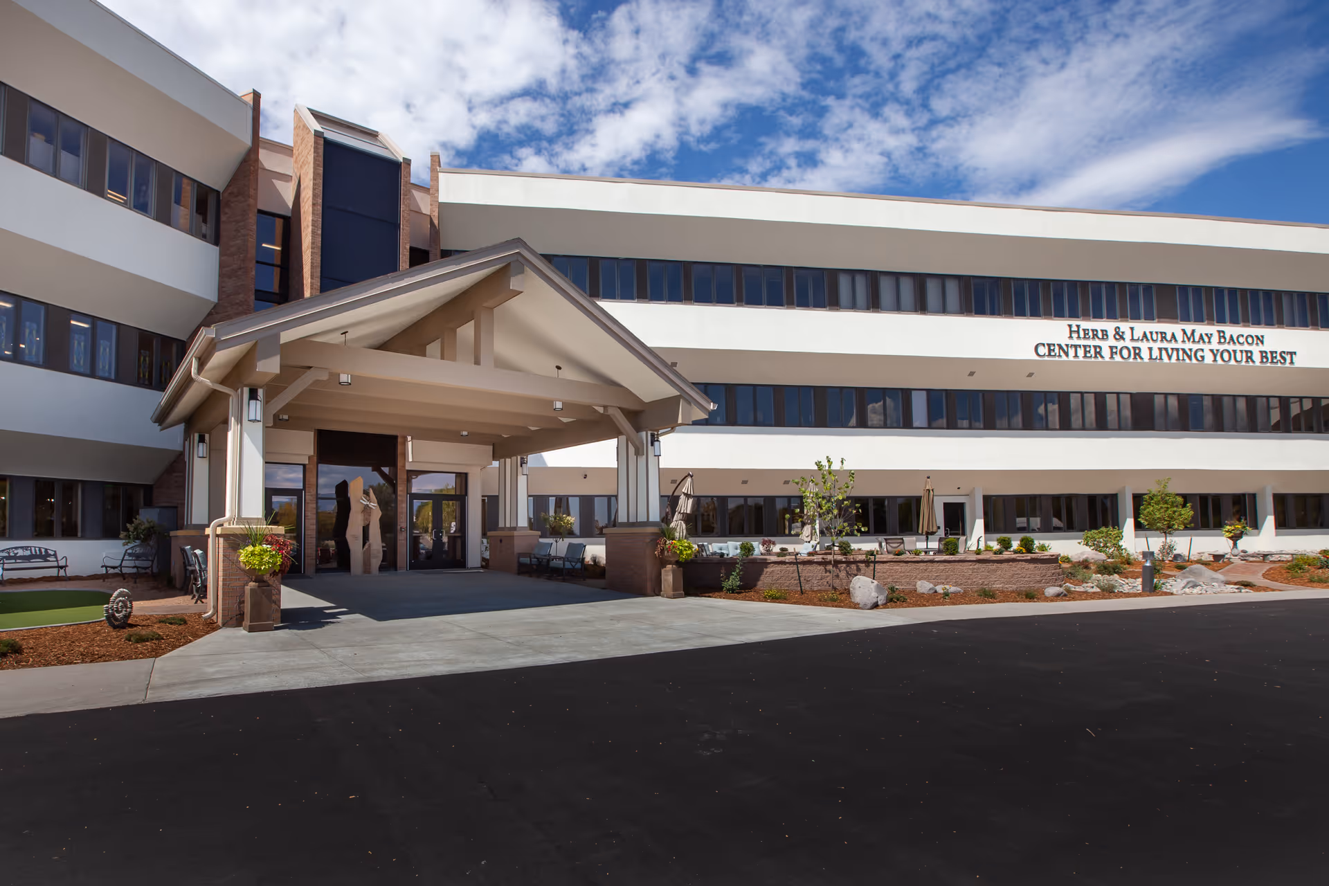 Modern senior living center with a covered entrance and landscaped front, under blue sky.
