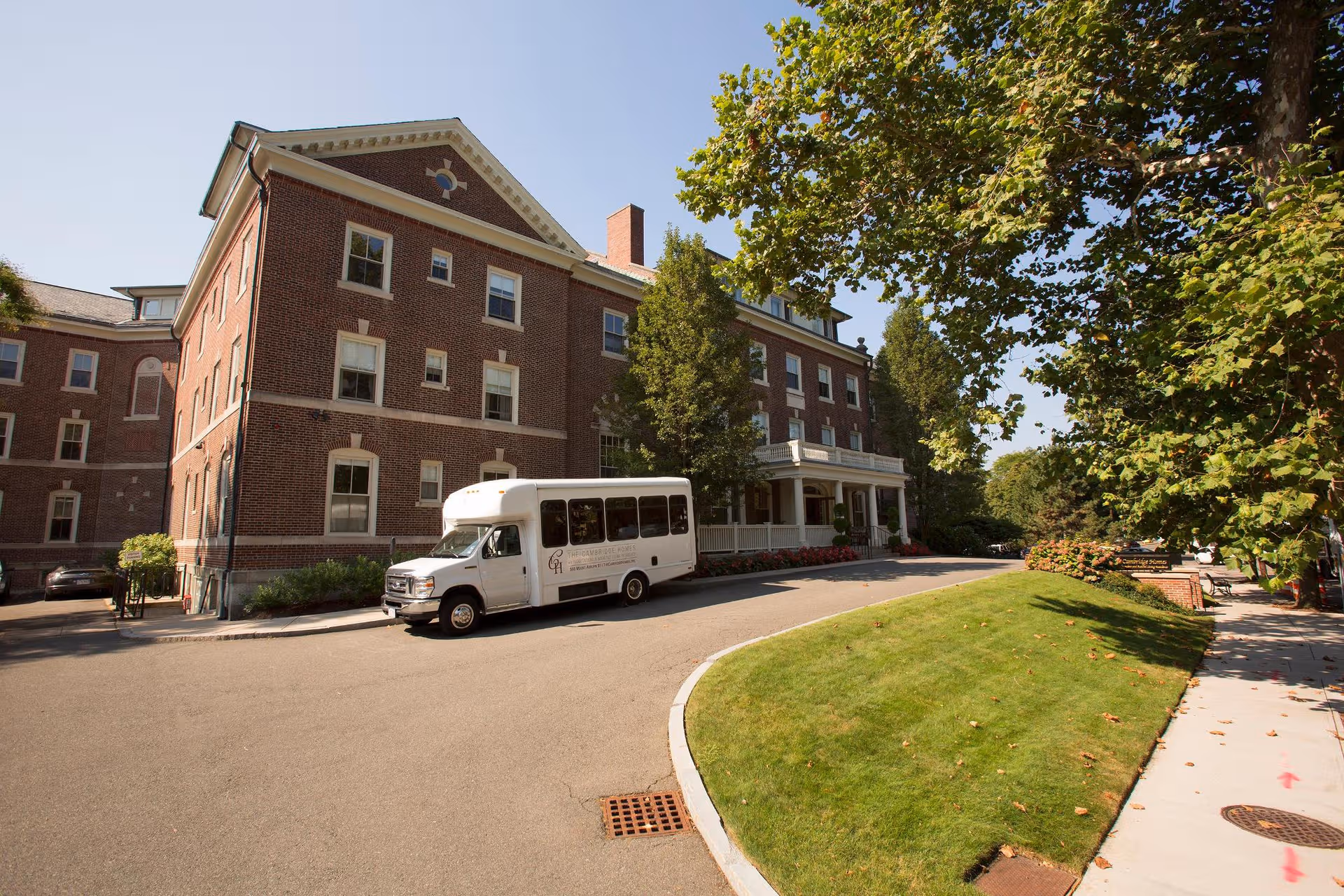 Brick senior living facility front with a white bus parked on the driveway and green lawn.