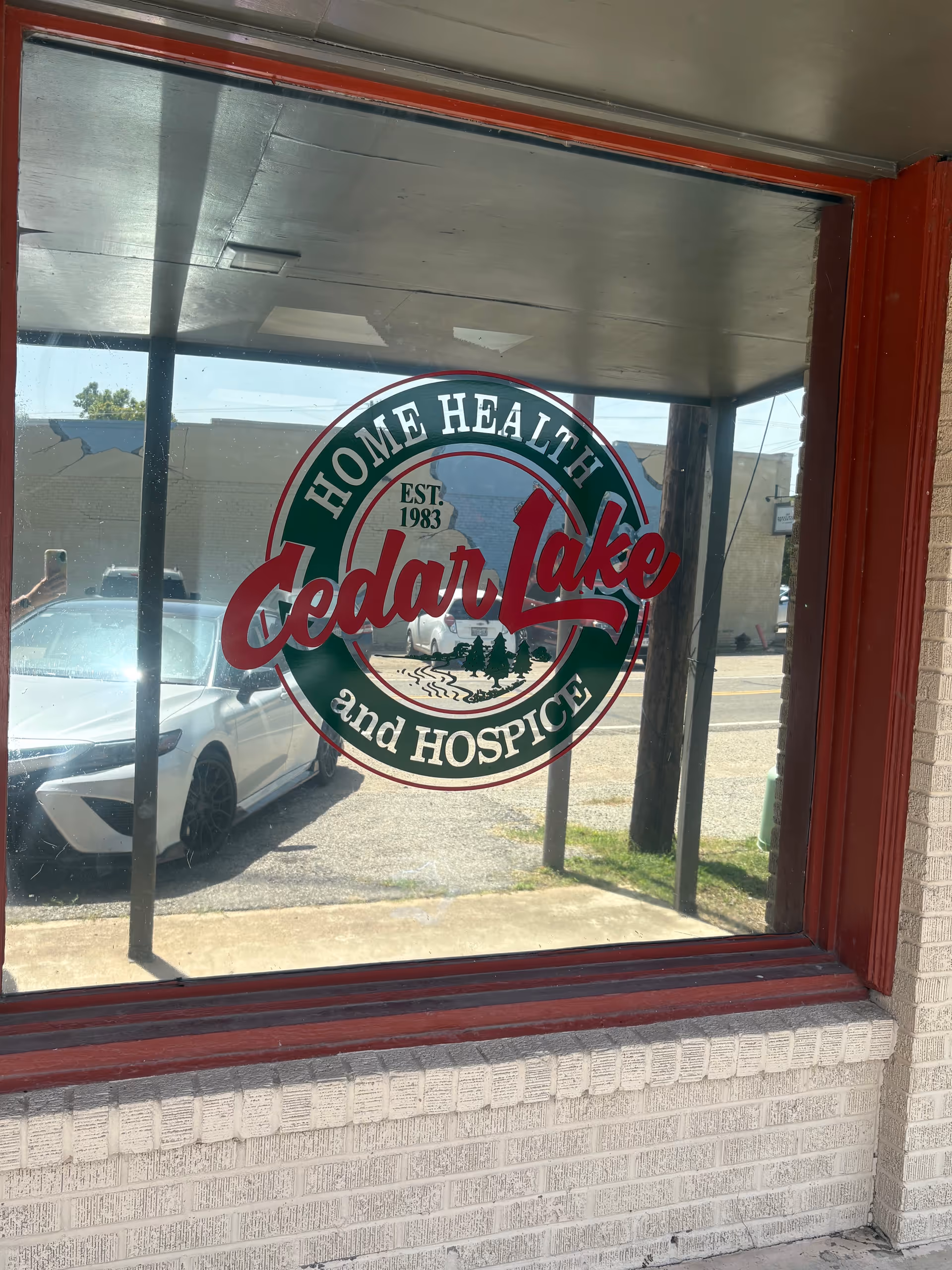 Window displays Cedar Lake Home Health and Hospice logo with a car outside.