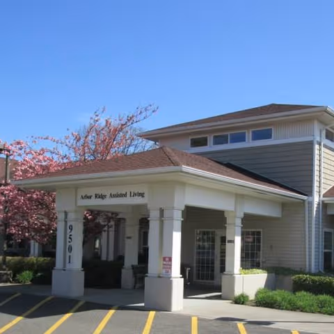 Front view of Arbor Ridge Assisted Living entrance with pillars and flowering trees.