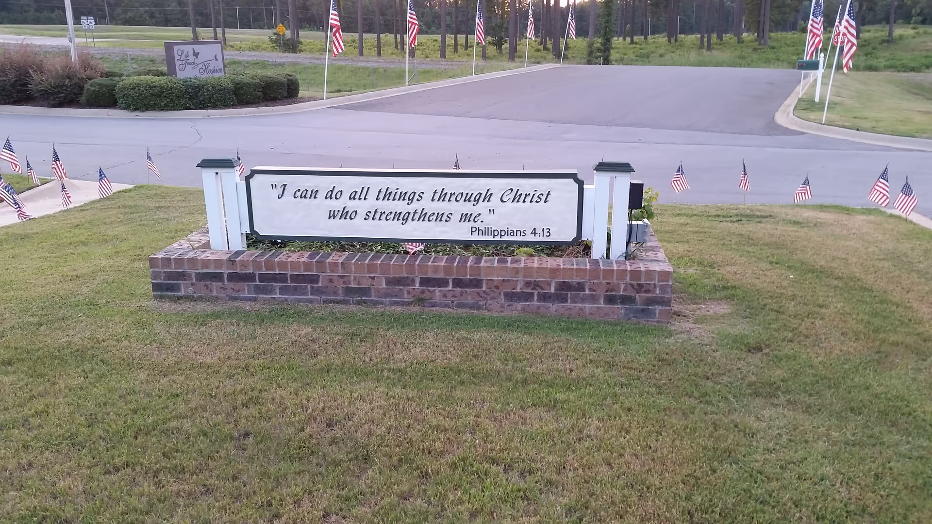 Brick planter with a sign and American flags at the entrance of Life Touch Hospice.