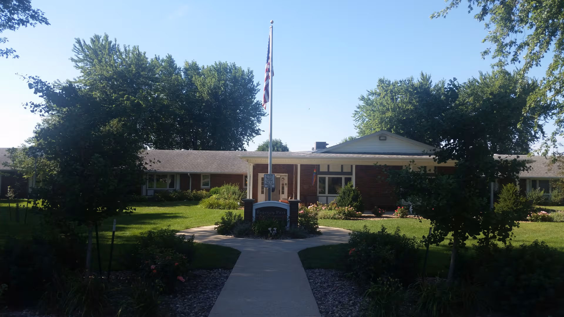 Front view of Regency Park Nursing and Rehab Center with flagpole and landscaped walkway.