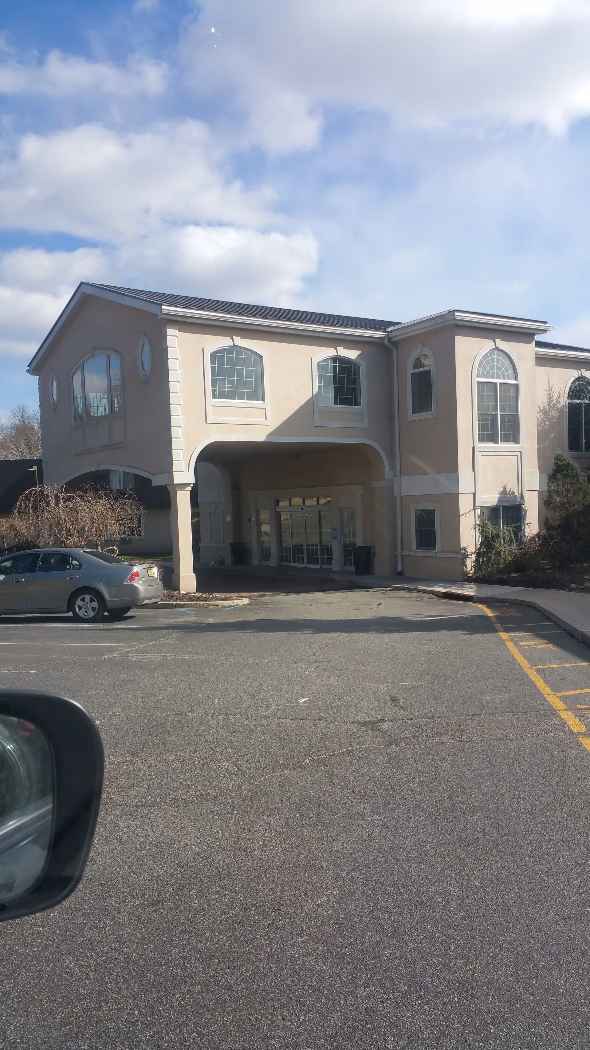 Exterior view of Lincoln Park Care Center: two-story beige building with arched entrance and parking lot.