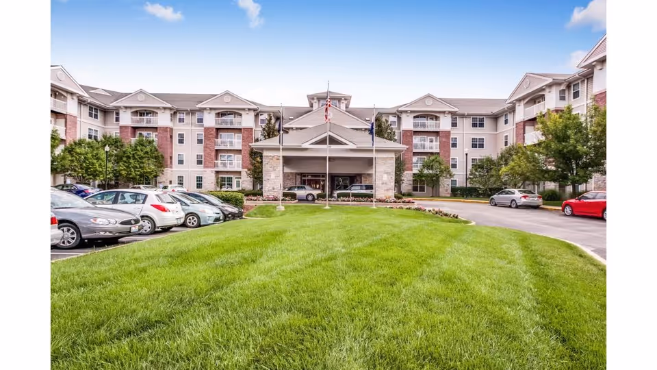Exterior view of Fairwinds River's Edge showing a central entrance, green lawn, and parked cars.