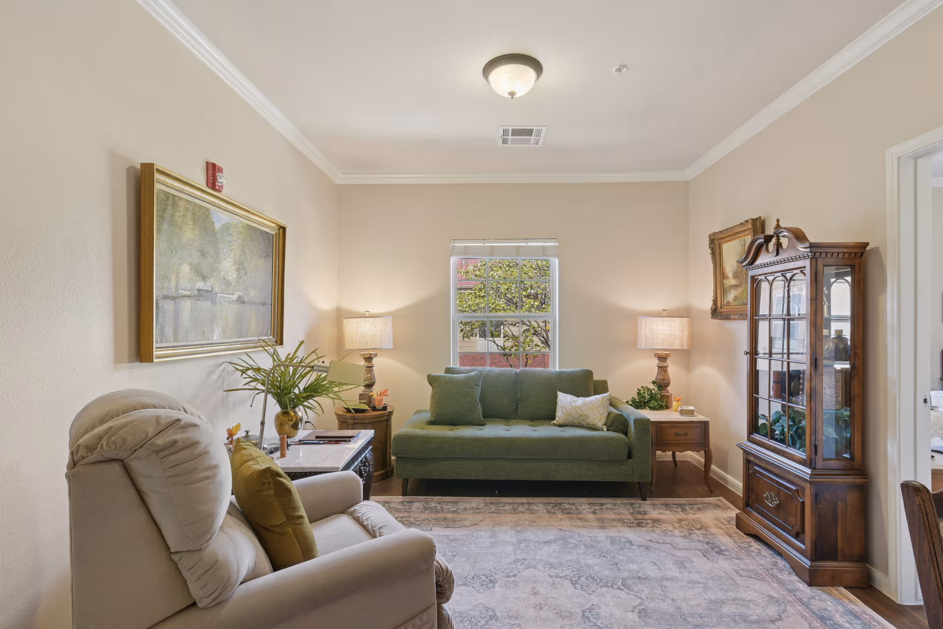 Cozy living room with green sofa, lamps, and a wooden glass display cabinet.