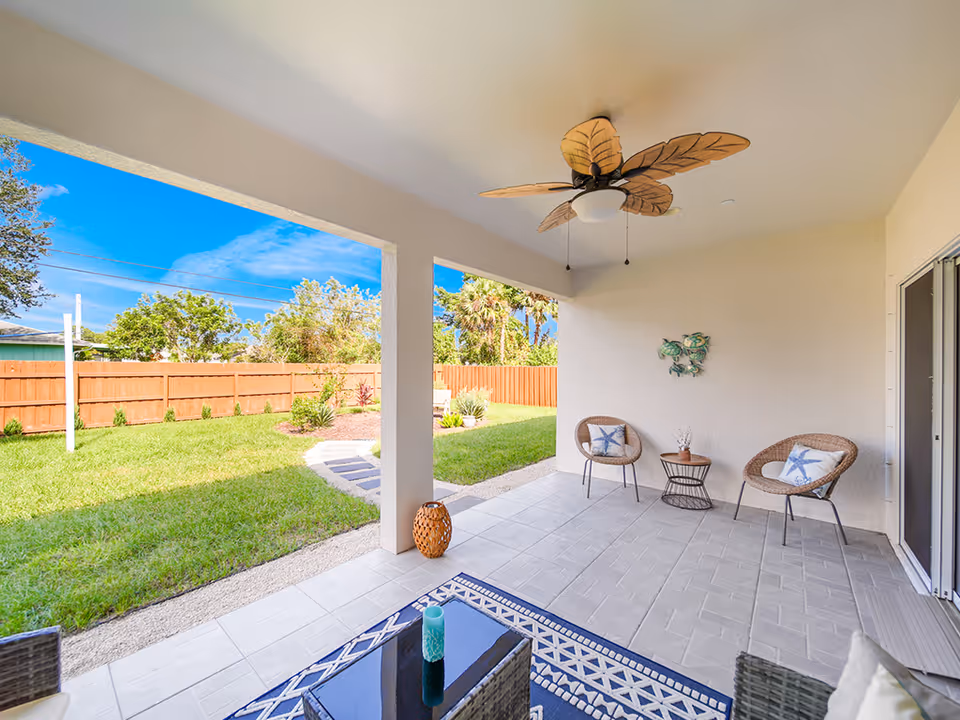 Cozy outdoor patio with two chairs, a ceiling fan, and a view of a fenced backyard.