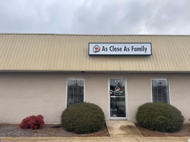 Exterior view of a beige senior living building with a sign reading 'As Close As Family'.