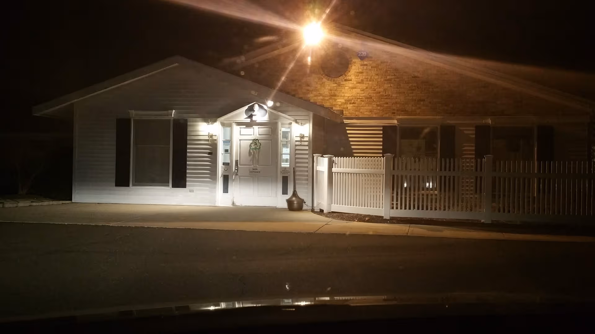 Evening exterior view of Apple Rehab Avon entrance with a white door and fencing.