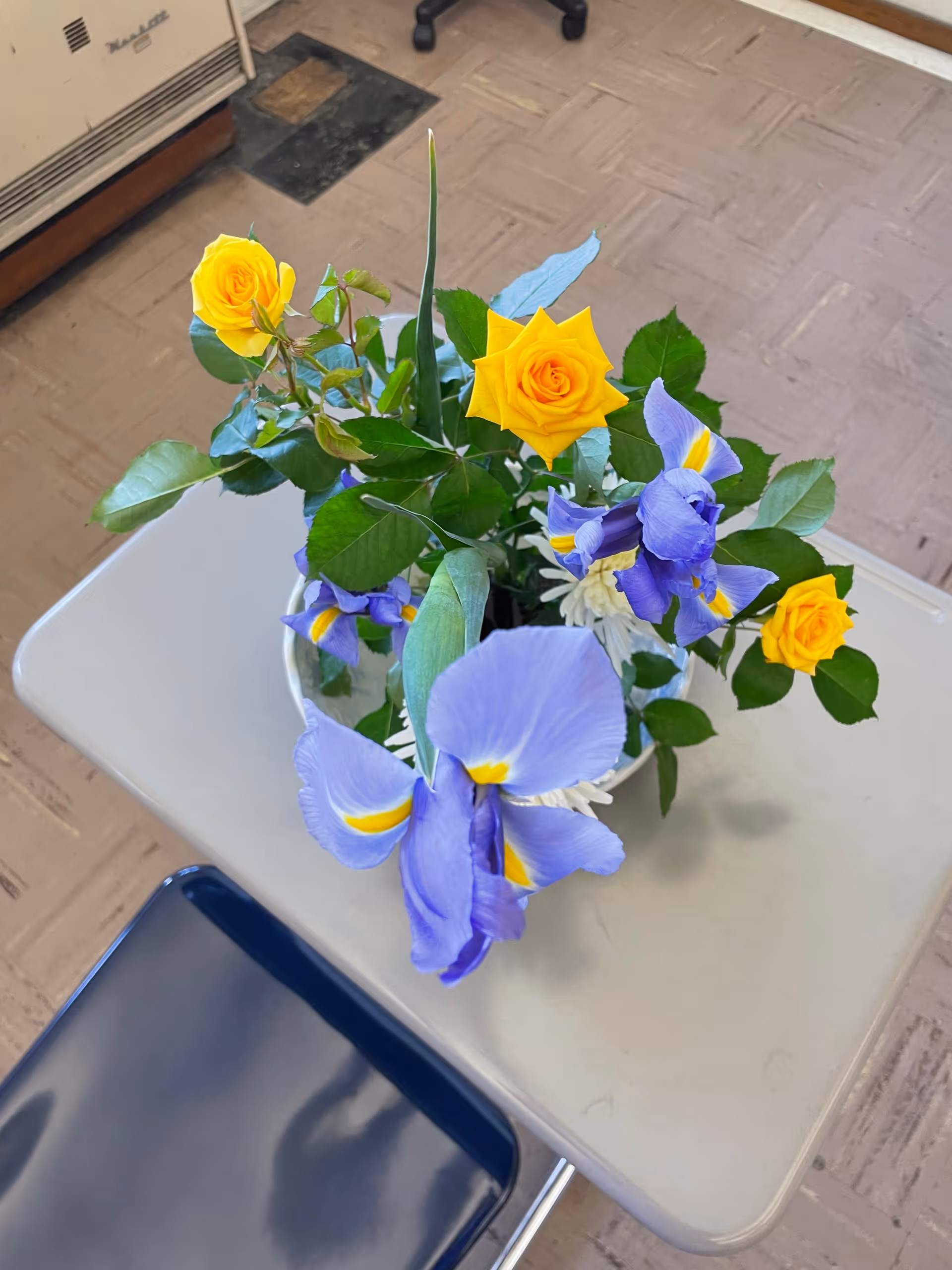 A colorful bouquet of yellow roses and purple irises on a small beige table.