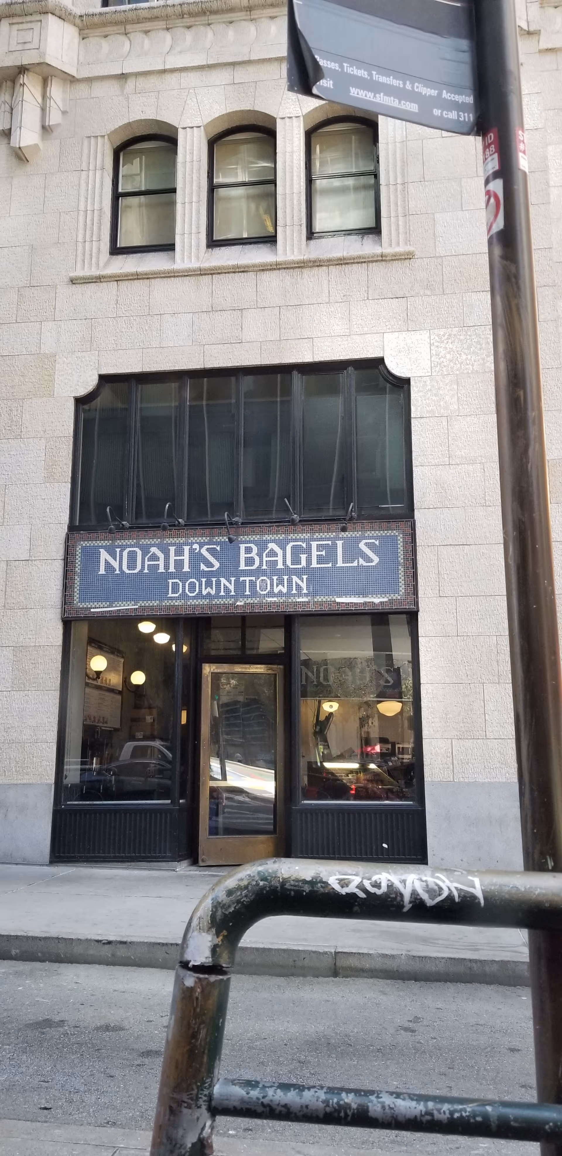Downtown storefront of Noah's Bagels with glass doors and sidewalk in front.