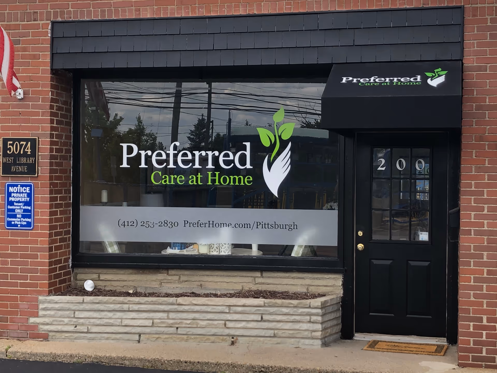 Brick storefront with large Preferred Care at Home sign on window and black door.