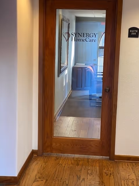 Wood-framed glass door in a hallway labeled SYNERGY HomeCare, with suite 205 sign.
