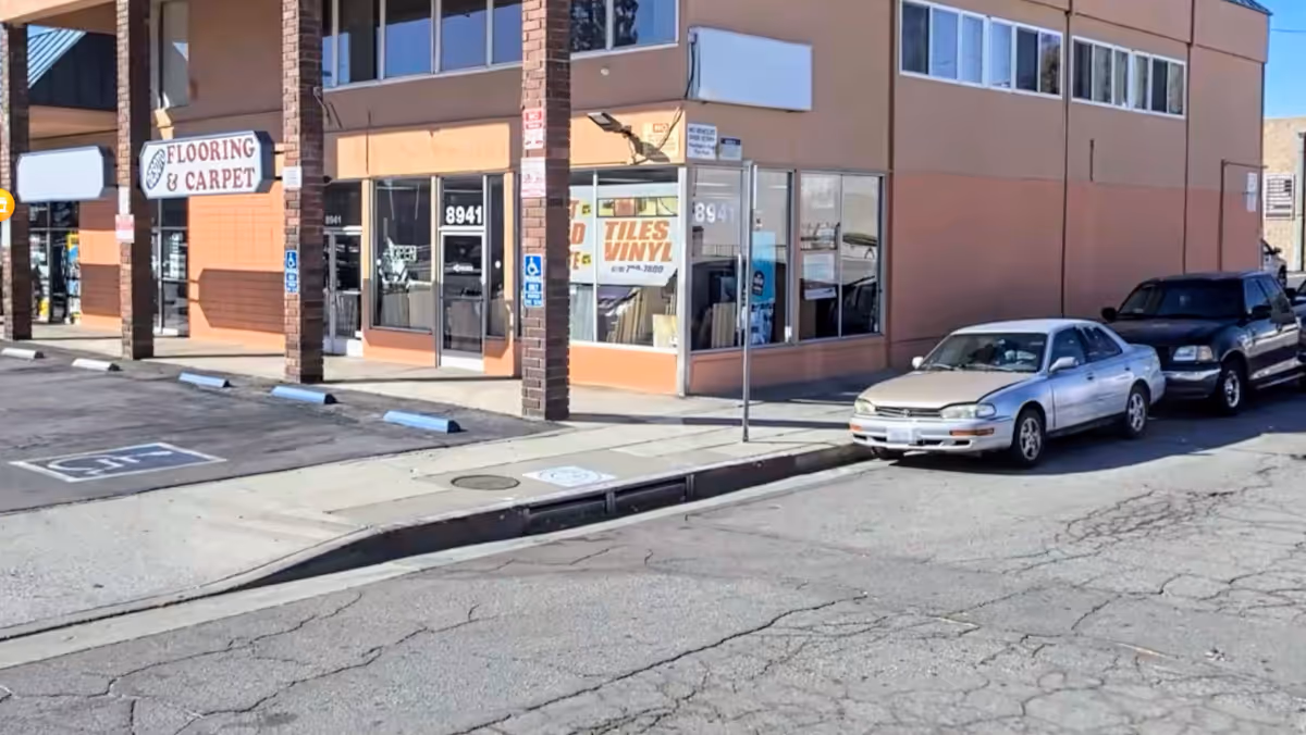 Corner storefront building with Flooring & Carpet sign, large glass windows, and parked cars.
