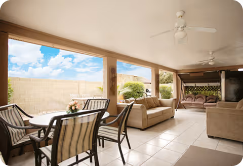 Covered outdoor seating area with tables, chairs, sofas, ceiling fans, and a bright yard view.