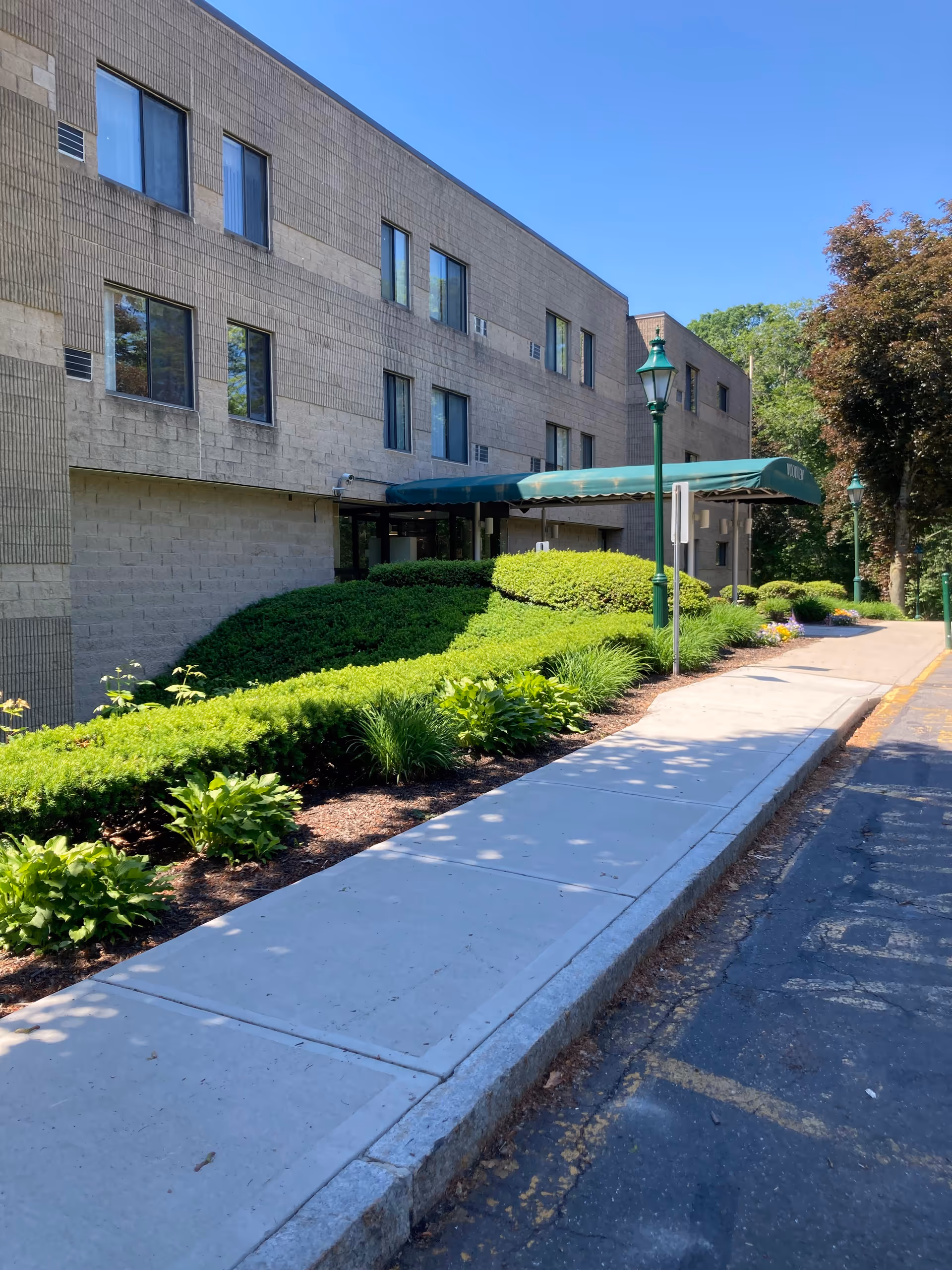 Exterior view of a brick senior living building with green landscaping and an entrance awning.