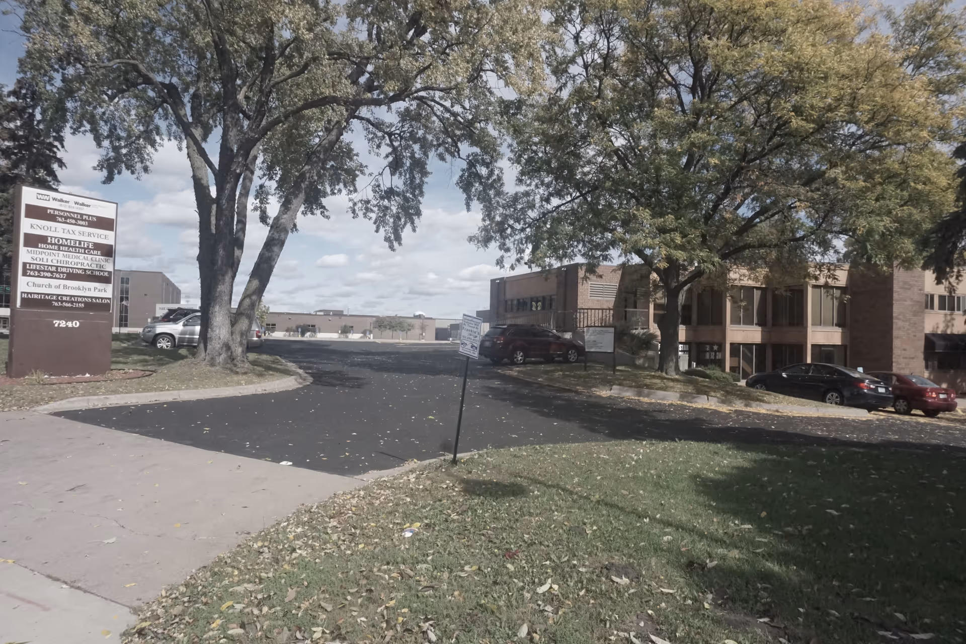 Exterior view of a brick senior living building with trees, parking lot, and a sign.