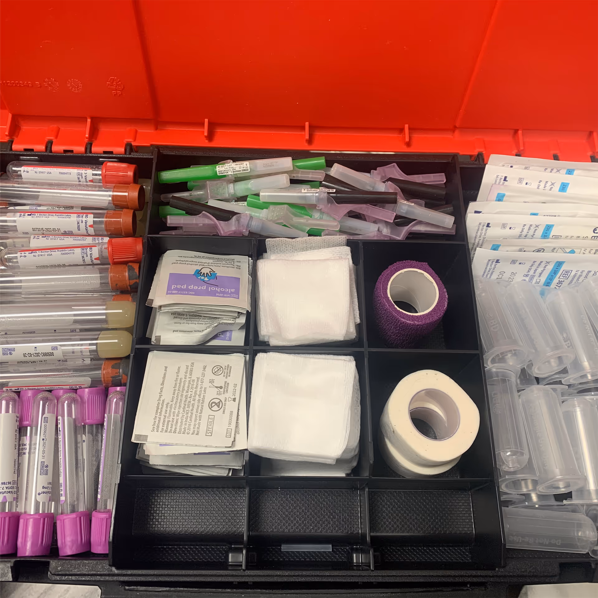 Open tray of medical supplies for blood draws, including syringes, tape, gauze, and bandages.