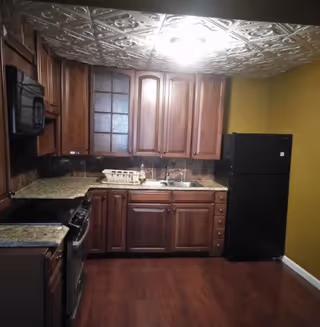 Compact kitchen with wooden cabinets, granite countertops, black appliances, and a decorative tin ceiling.