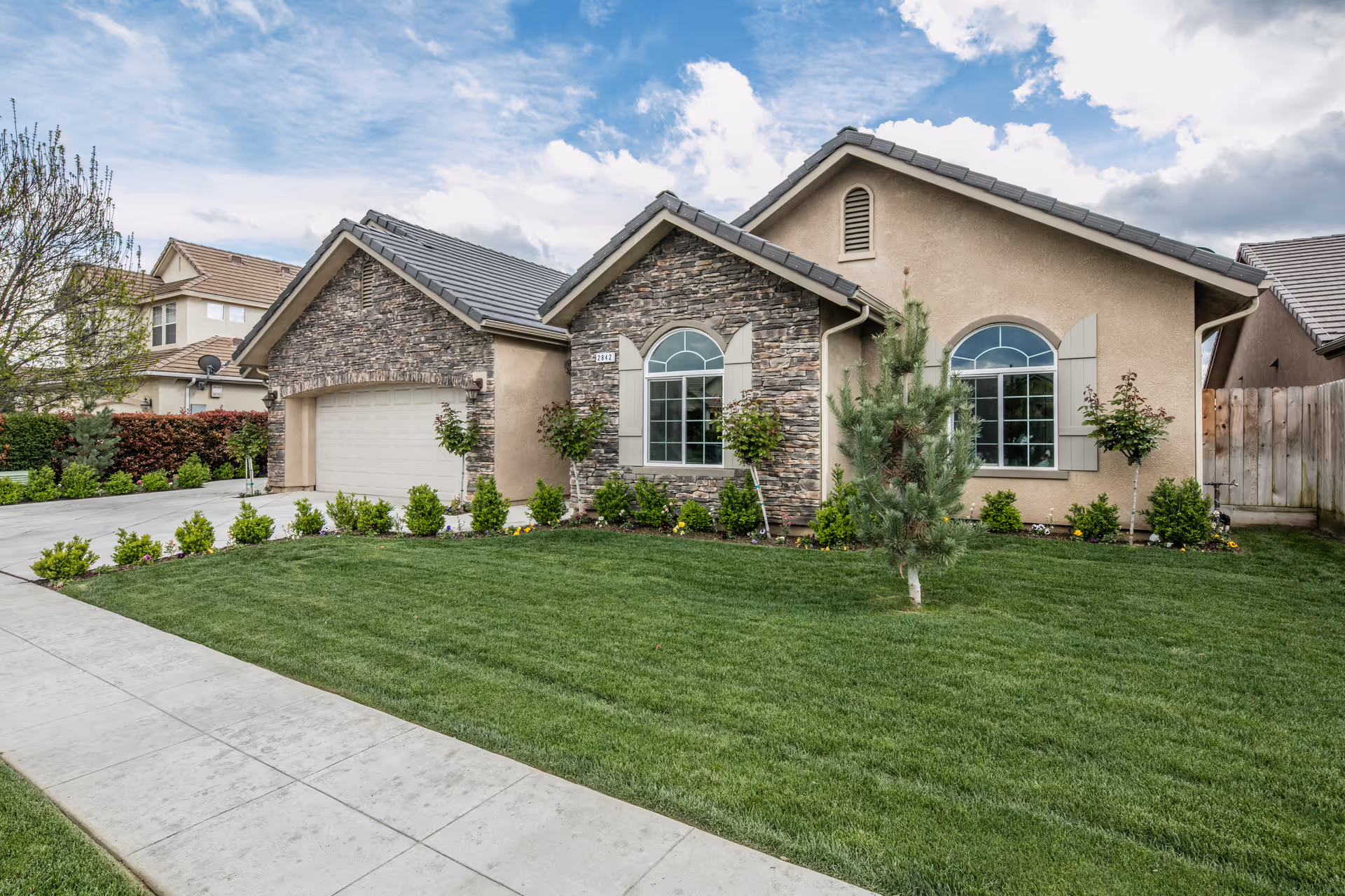 Front exterior of a beige residential home with manicured lawn and stone accents.