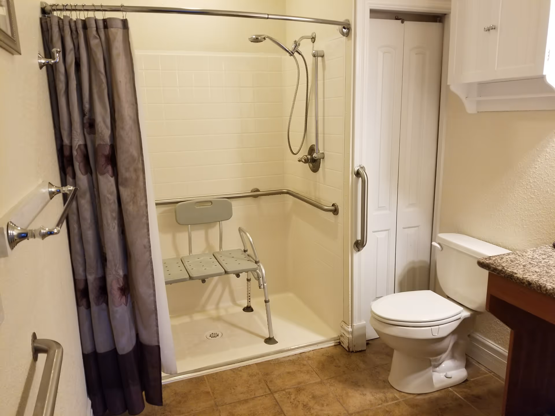 Accessible bathroom featuring a walk-in shower with chair, grab bars, and a toilet.