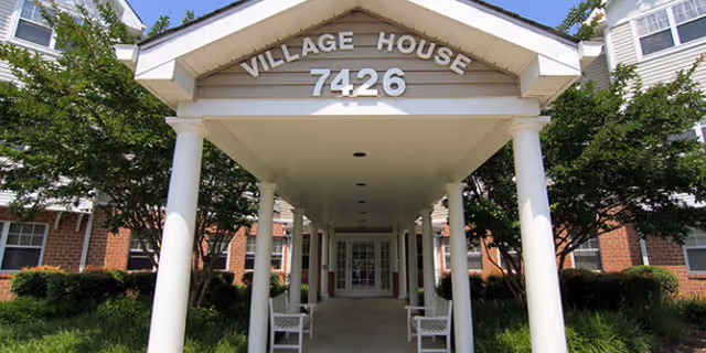 Front entrance of Village House Apartments with a covered walkway and white columns.
