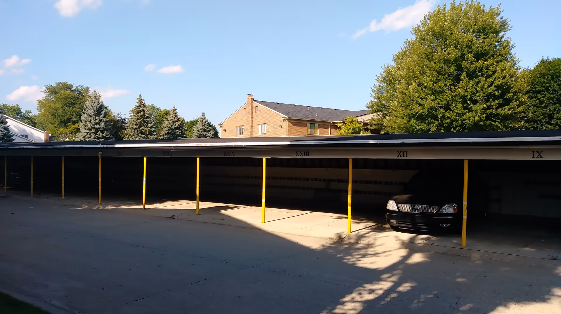 Exterior carport with yellow pillars and a parked car beside a building.