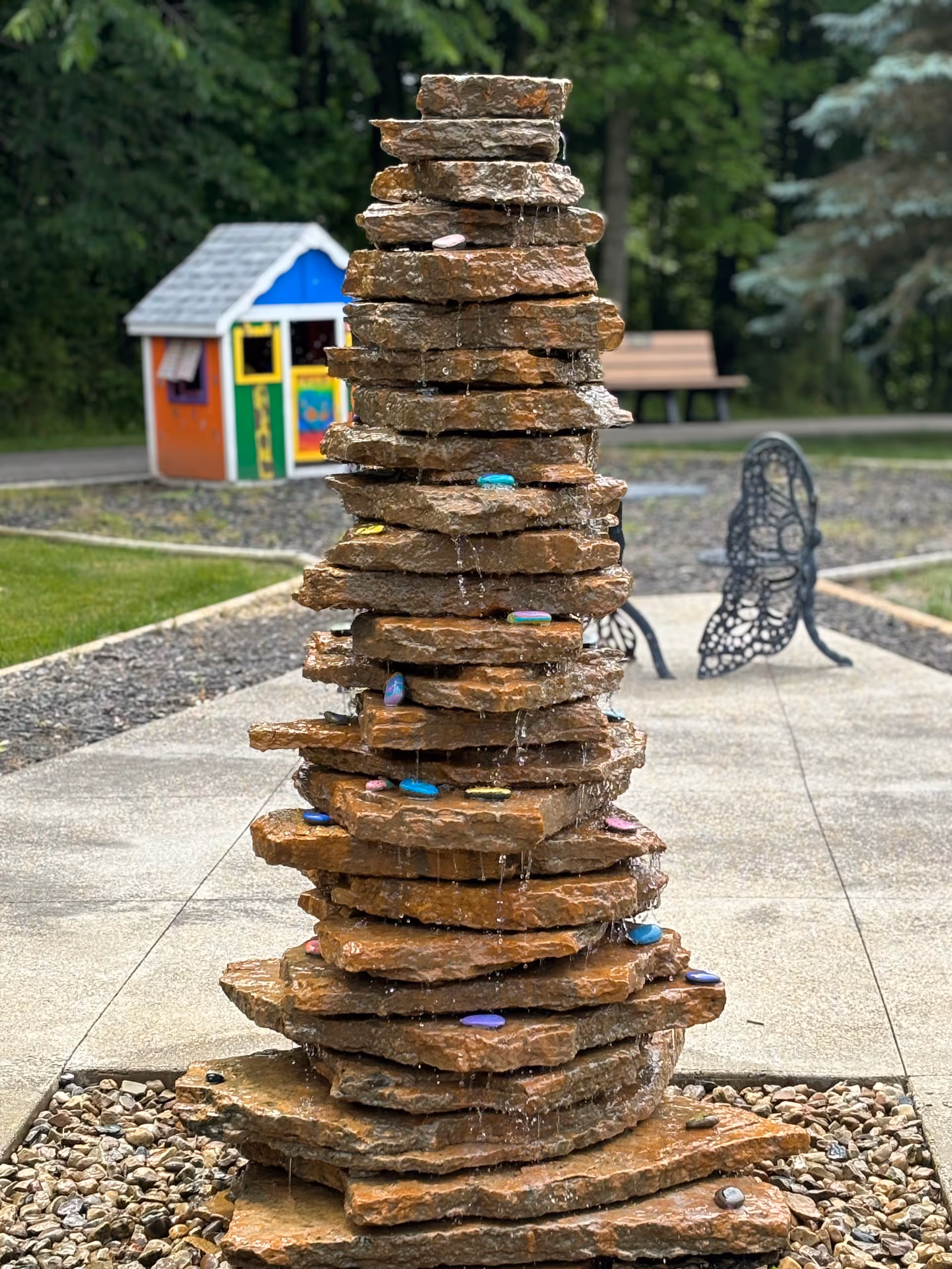 Stacked stone sculpture in an outdoor courtyard with a small colorful playhouse.