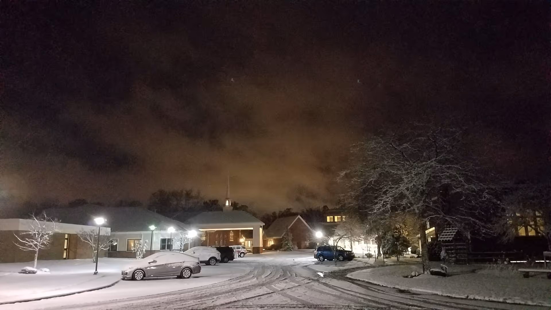 Night exterior of Wesbury United Methodist facility with snow-covered parking lot and cars