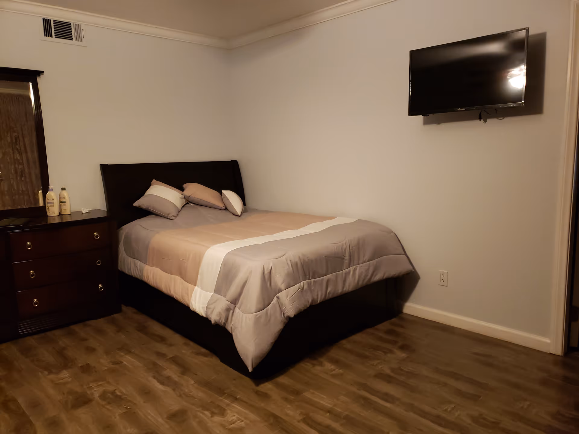 Bedroom with a large bed, dresser, wall-mounted TV, and wood-style flooring.