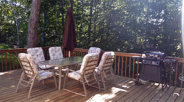 Outdoor wooden deck with a glass table, floral cushioned chairs, umbrella, and a grill.