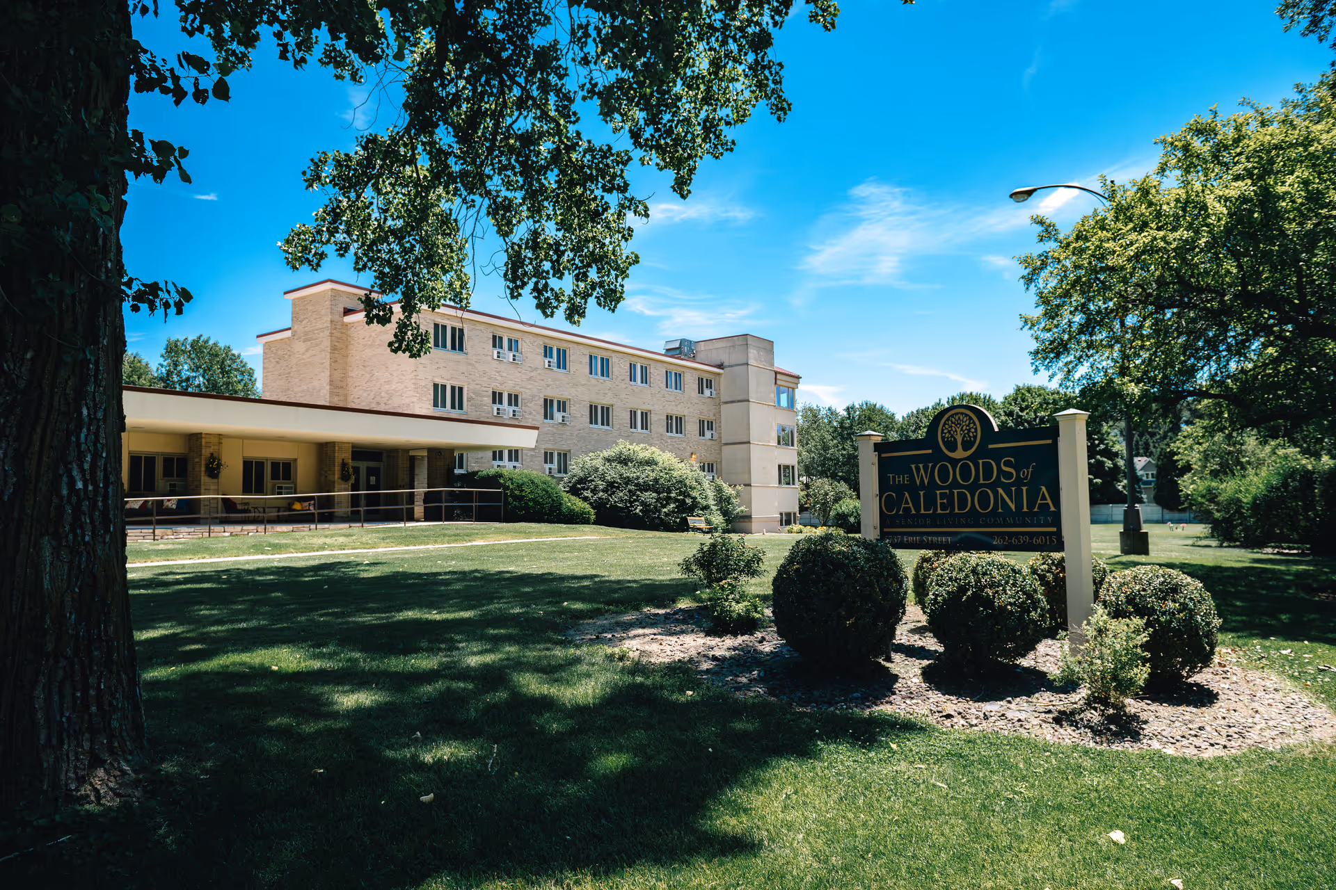 Exterior view of The Woods of Caledonia senior living facility with sign and landscaping.
