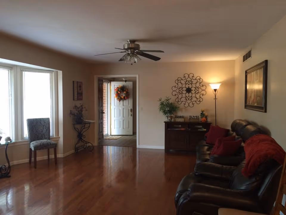 Spacious living room with leather recliners, hardwood floors, ceiling fan, and entry doorway.