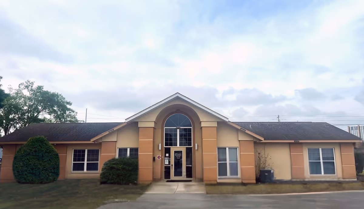 Front view of a single-story beige facility with central arched entrance.