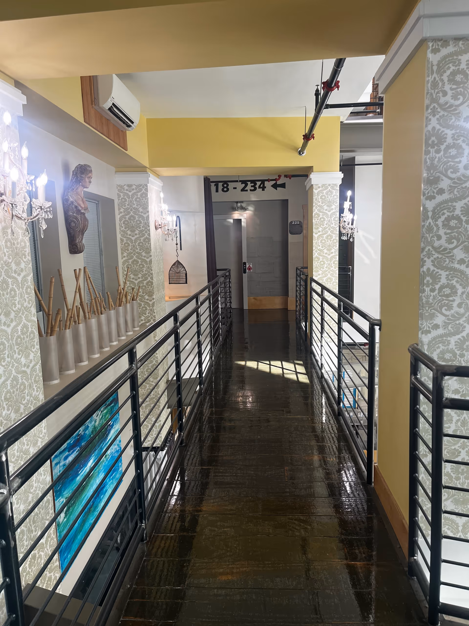 Interior corridor with glossy dark floor, decorative wallpaper, railings, and lighting.
