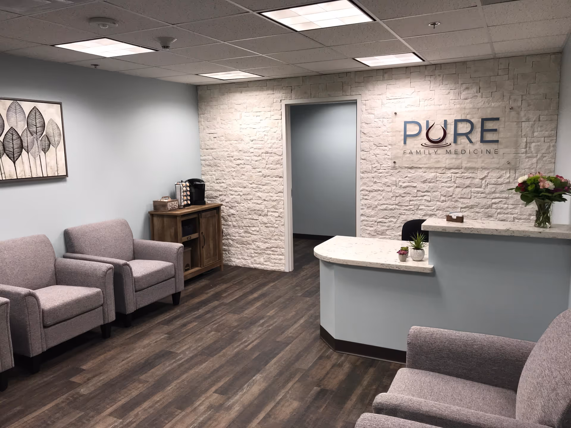 Reception area with gray chairs, a curved marble desk, and a Pure Family Medicine sign.